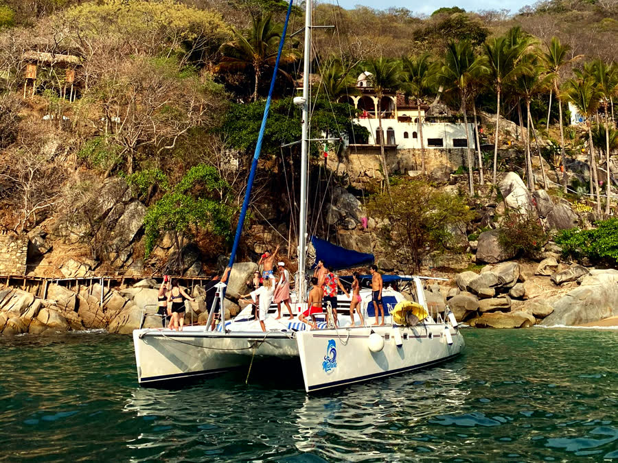 The catamaran at anchor below the hillside homes of the bay